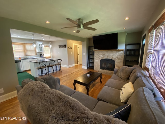 living room featuring a fireplace, light hardwood / wood-style flooring, sink, and ceiling fan