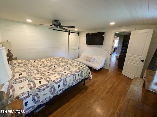 bedroom with dark wood-type flooring, ceiling fan, a barn door, and wooden walls