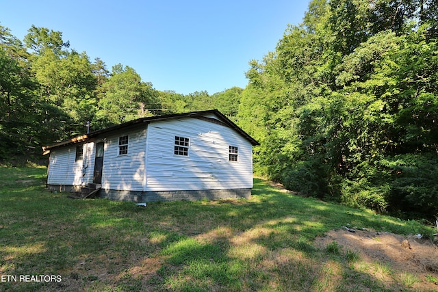 view of home's exterior featuring a lawn, a forest view, and entry steps