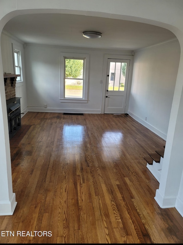 unfurnished living room with dark wood-type flooring, crown molding, plenty of natural light, and a fireplace