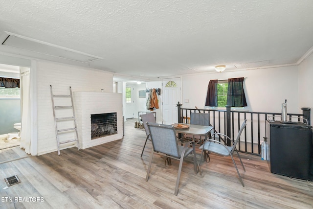 dining area with a textured ceiling, wood-type flooring, and a brick fireplace