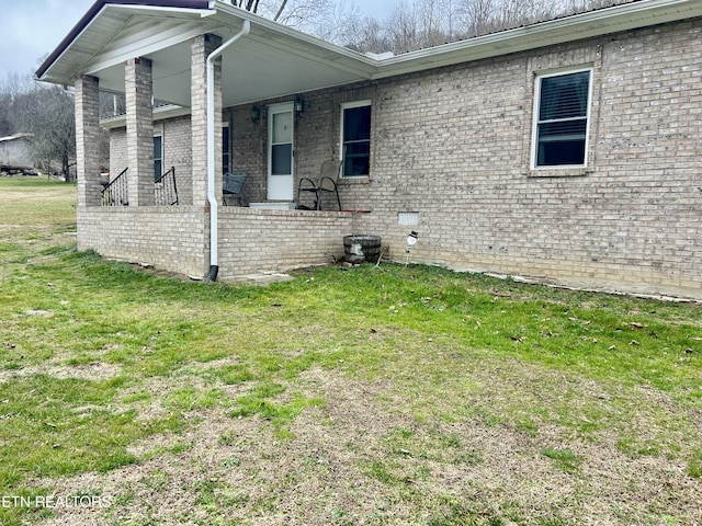 view of side of home with brick siding, covered porch, and a lawn