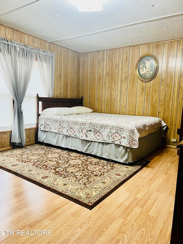 bedroom with wood walls, a textured ceiling, and light wood-type flooring