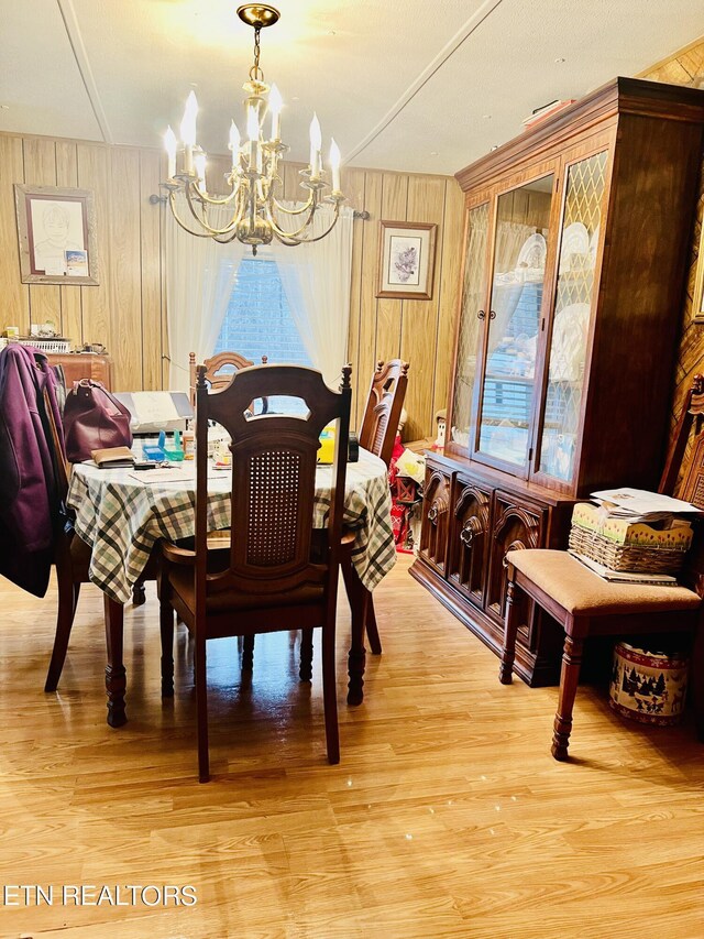 dining room featuring wood walls, light hardwood / wood-style flooring, and an inviting chandelier