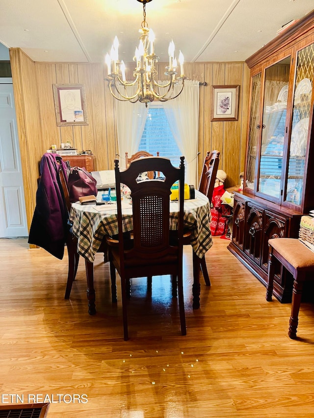 dining area with a chandelier, a healthy amount of sunlight, wooden walls, and light wood-type flooring