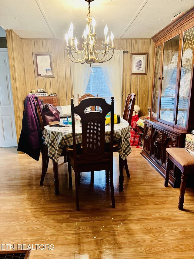 dining area with a notable chandelier, light wood-style floors, and wood walls