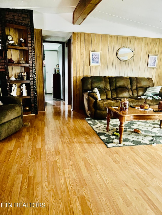 living room featuring wood walls, vaulted ceiling with beams, and light wood-type flooring