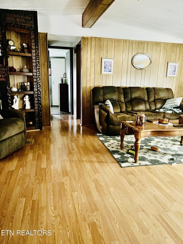 living area featuring beam ceiling, wooden walls, and wood finished floors