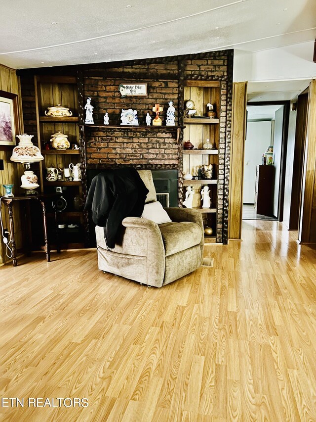 living room featuring a textured ceiling, light hardwood / wood-style flooring, a brick fireplace, and built in shelves