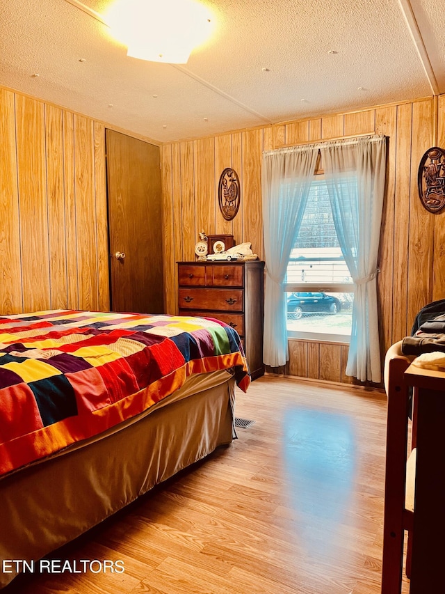 bedroom with wood walls, a textured ceiling, and wood finished floors