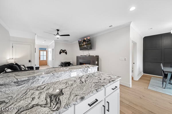 interior space featuring light wood-type flooring, crown molding, light stone countertops, ceiling fan, and white cabinets