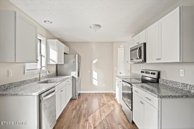 kitchen featuring appliances with stainless steel finishes, sink, white cabinets, and light stone counters