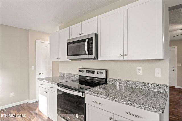 kitchen with appliances with stainless steel finishes, light stone counters, a textured ceiling, white cabinets, and dark hardwood / wood-style flooring