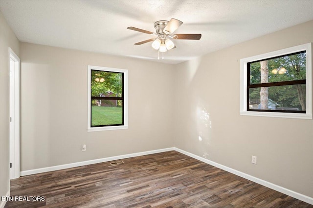 empty room featuring dark wood-type flooring, a wealth of natural light, a textured ceiling, and ceiling fan