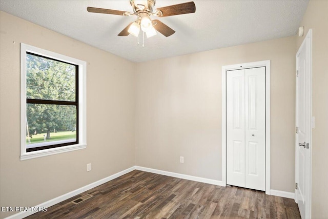 unfurnished bedroom with ceiling fan, a textured ceiling, dark hardwood / wood-style flooring, and a closet