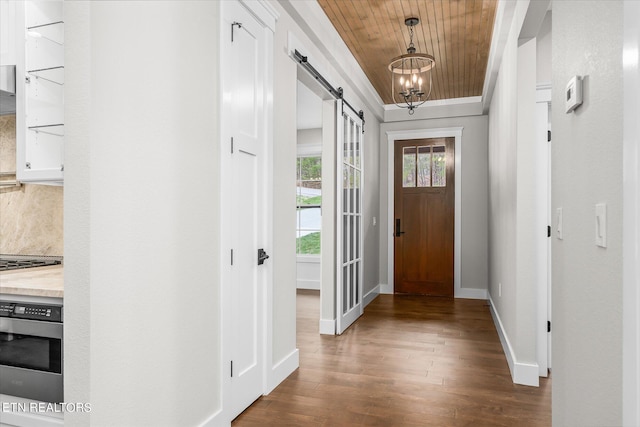 foyer entrance featuring wood ceiling, dark wood-type flooring, a notable chandelier, ornamental molding, and a barn door