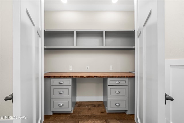 unfurnished office featuring built in desk and dark hardwood / wood-style flooring