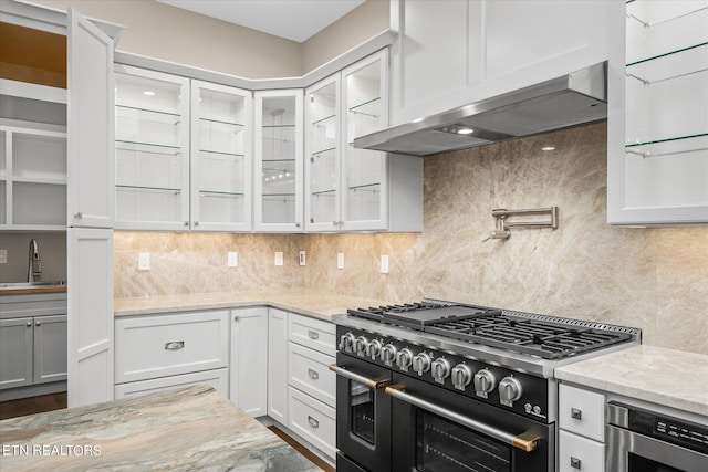 kitchen with white cabinetry, wall chimney exhaust hood, light stone countertops, and range with two ovens