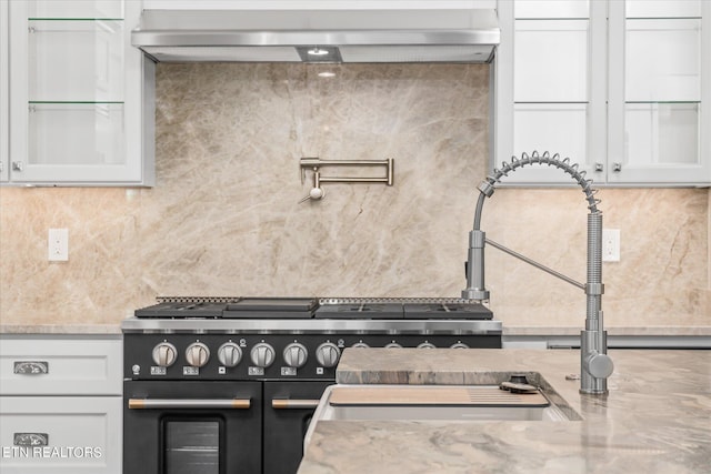 interior details featuring double oven range, light stone countertops, white cabinets, and backsplash