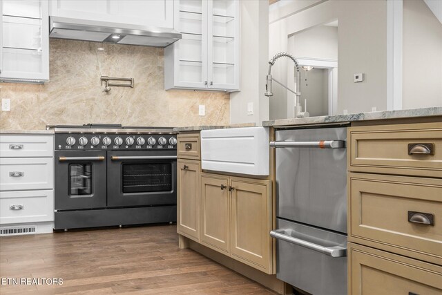 kitchen with exhaust hood, light stone counters, double oven range, hardwood / wood-style floors, and backsplash