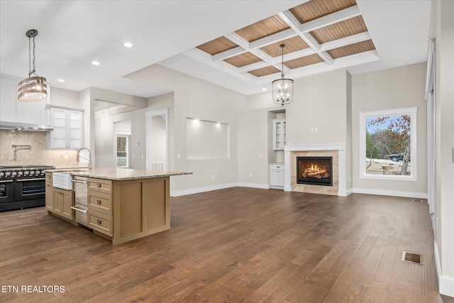 kitchen with stove, light stone counters, backsplash, a kitchen island, and coffered ceiling