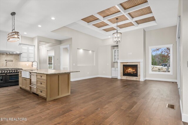 kitchen featuring decorative light fixtures, a center island with sink, double oven range, light stone countertops, and decorative backsplash
