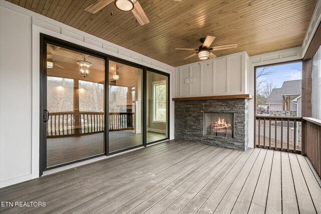 unfurnished sunroom with wooden ceiling, a stone fireplace, and ceiling fan