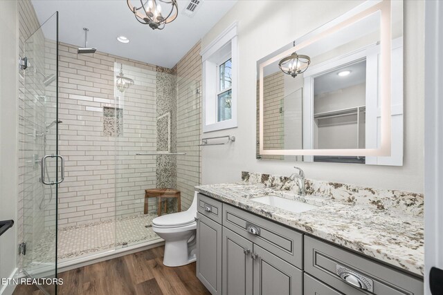 bathroom with a notable chandelier, vanity, hardwood / wood-style flooring, an enclosed shower, and toilet