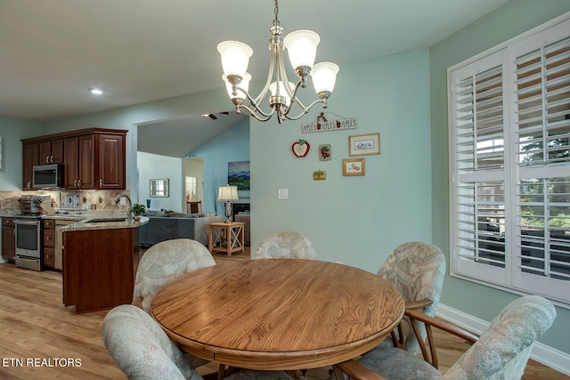 dining area featuring a notable chandelier, light wood-type flooring, sink, and vaulted ceiling