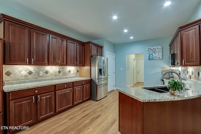 kitchen featuring light stone countertops, stainless steel fridge, light hardwood / wood-style floors, and backsplash