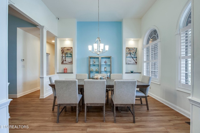 dining space with decorative columns, wood-type flooring, and an inviting chandelier