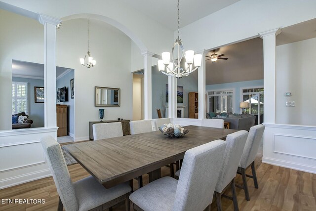 dining area featuring ceiling fan with notable chandelier, decorative columns, hardwood / wood-style flooring, and a high ceiling