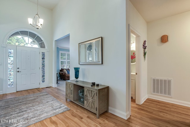 entryway with a towering ceiling, a chandelier, and light hardwood / wood-style floors