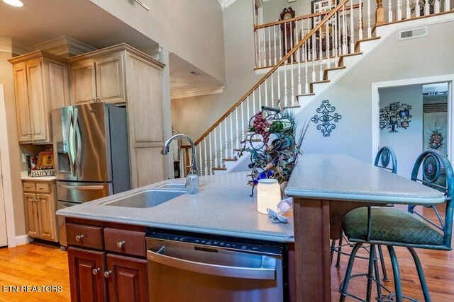 kitchen featuring a high ceiling, stainless steel appliances, crown molding, light wood-type flooring, and sink