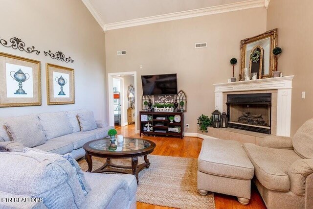 living room featuring light hardwood / wood-style floors, a tiled fireplace, crown molding, and a high ceiling