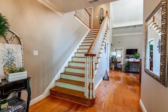 staircase featuring hardwood / wood-style flooring, a towering ceiling, and ornamental molding