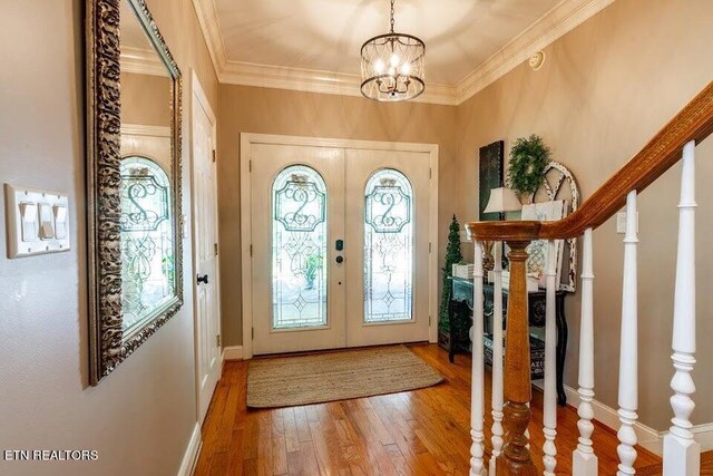 entrance foyer featuring ornamental molding, a notable chandelier, wood-type flooring, and french doors