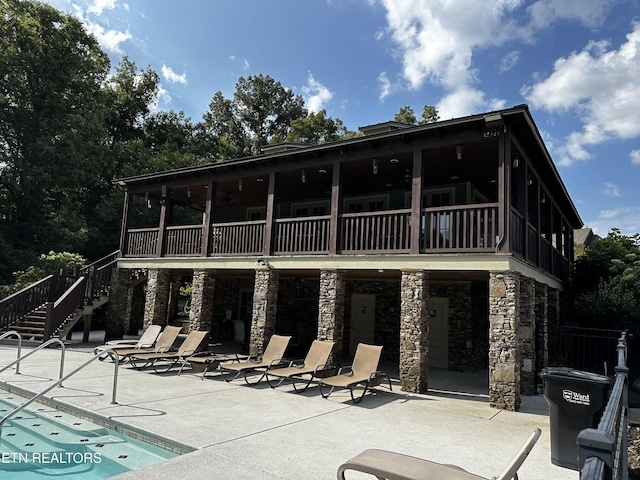 rear view of property featuring stairway, a community pool, a sunroom, a patio area, and stone siding