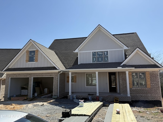 view of front of house with brick siding, covered porch, board and batten siding, and roof with shingles