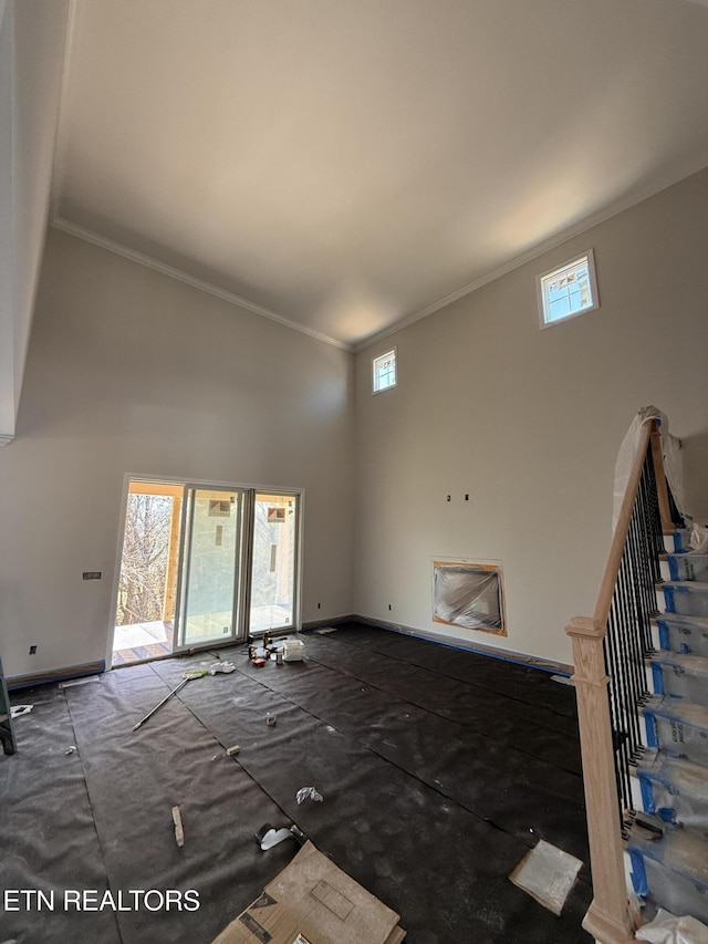 unfurnished living room featuring stairway, baseboards, a towering ceiling, and ornamental molding