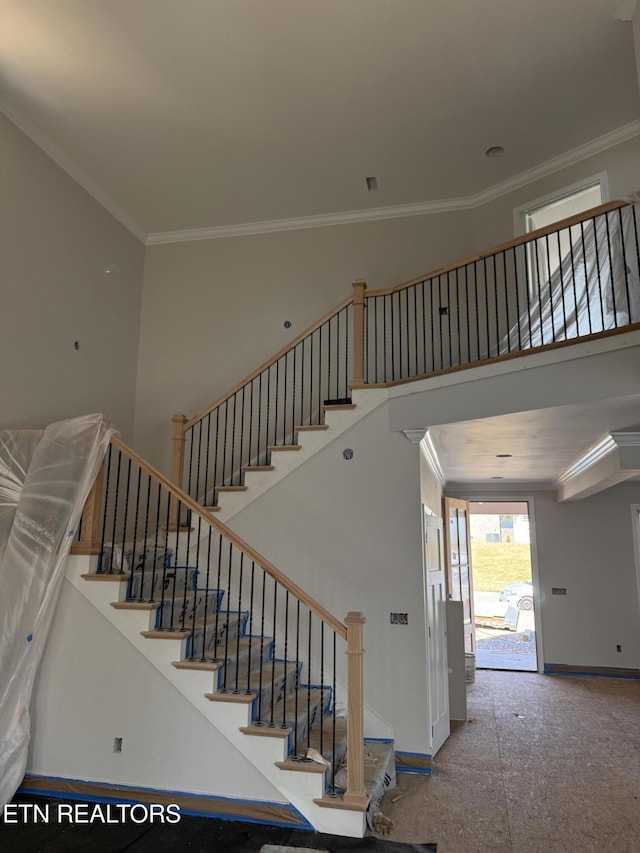 stairway featuring baseboards, a towering ceiling, and crown molding