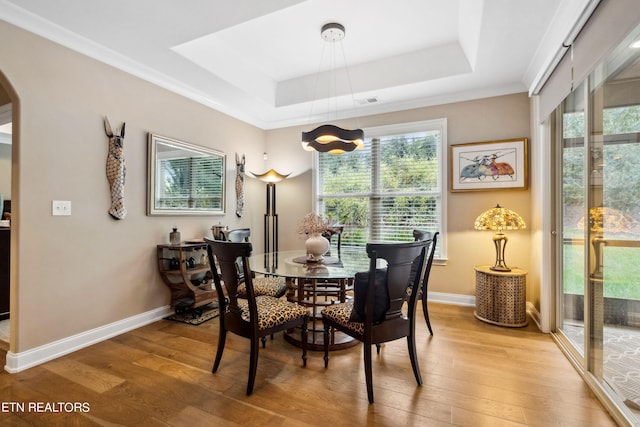 dining area with arched walkways, a tray ceiling, and wood finished floors