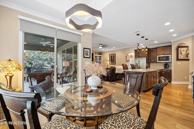 dining room featuring ornamental molding, arched walkways, light wood-style floors, and ceiling fan