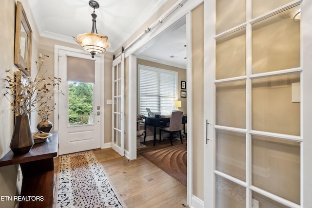 entrance foyer with baseboards, a barn door, wood finished floors, and crown molding