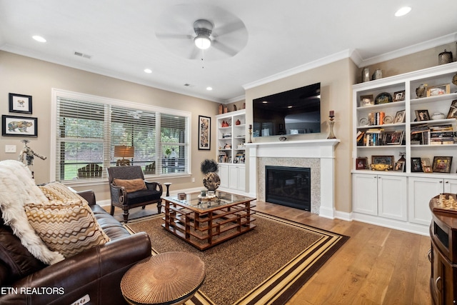 living area featuring recessed lighting, visible vents, ornamental molding, light wood-type flooring, and a glass covered fireplace