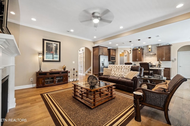 living area featuring baseboards, arched walkways, crown molding, light wood-type flooring, and a high end fireplace