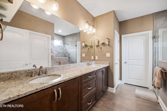 full bath featuring double vanity, a shower stall, baseboards, and a sink