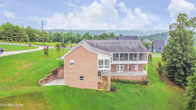 exterior space with a patio, a sunroom, a lawn, and a mountain view