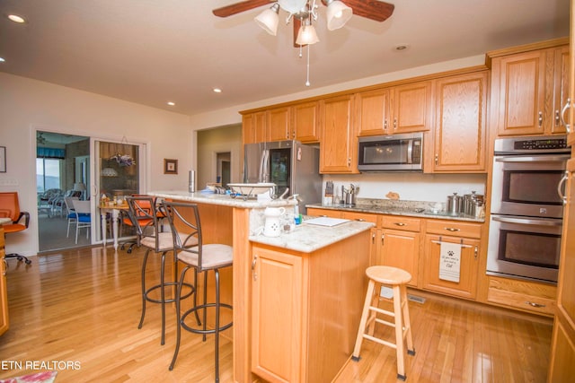 kitchen with stainless steel appliances, a center island, a kitchen bar, light wood-type flooring, and ceiling fan