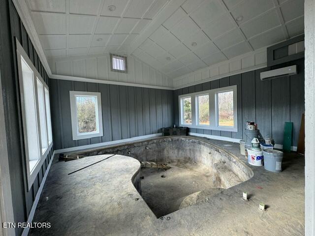 interior space with a wall mounted air conditioner, lofted ceiling, and a healthy amount of sunlight